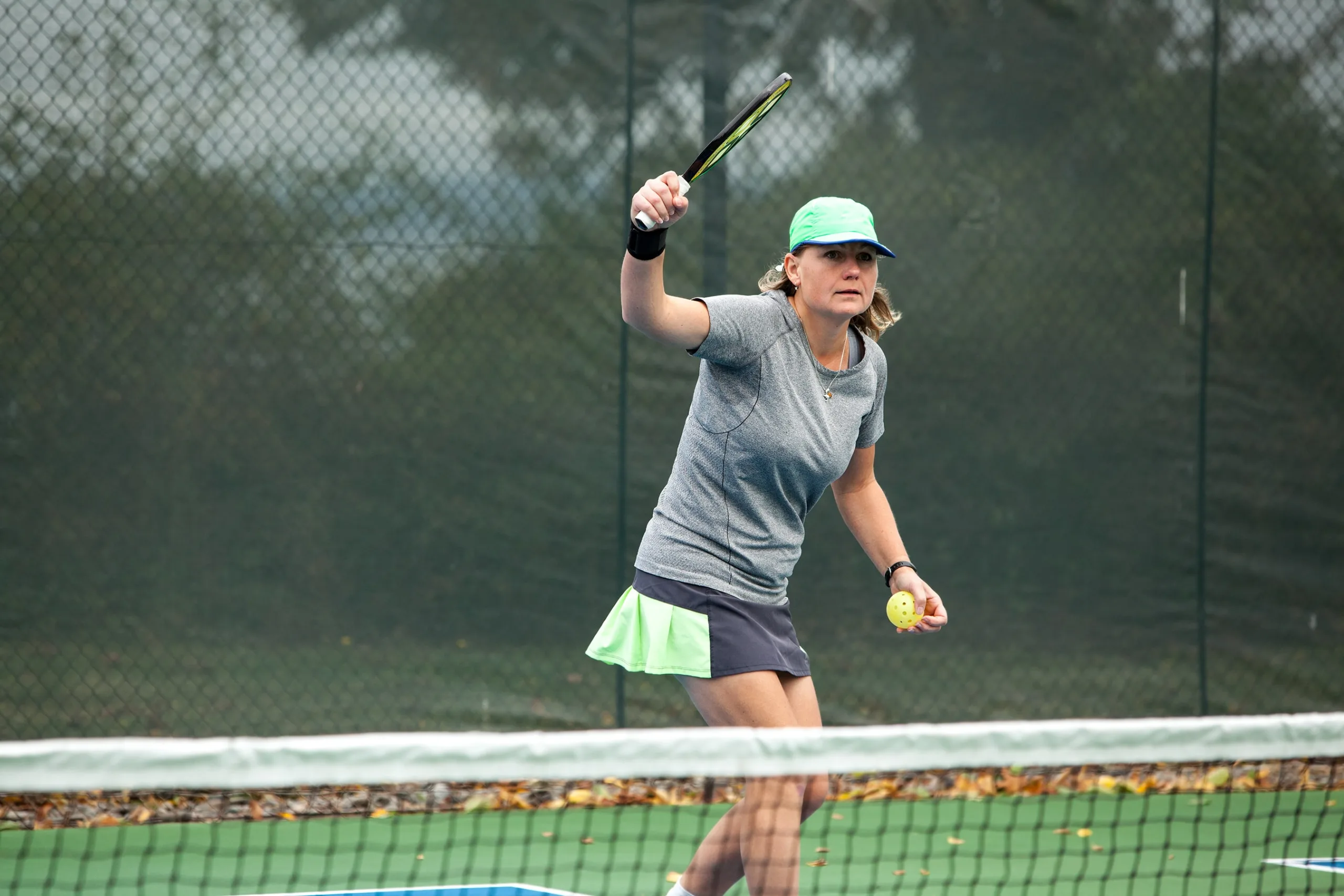 Woman serving a pickleball game wearing a green tennis hat, grey shirt, and black and lime green skirt. New pet-friendly apartment homes for rent with private fenced backyards in Kissimmee, FL, near Orlando, FL with pickle ball, dog park, gym, and gated community.